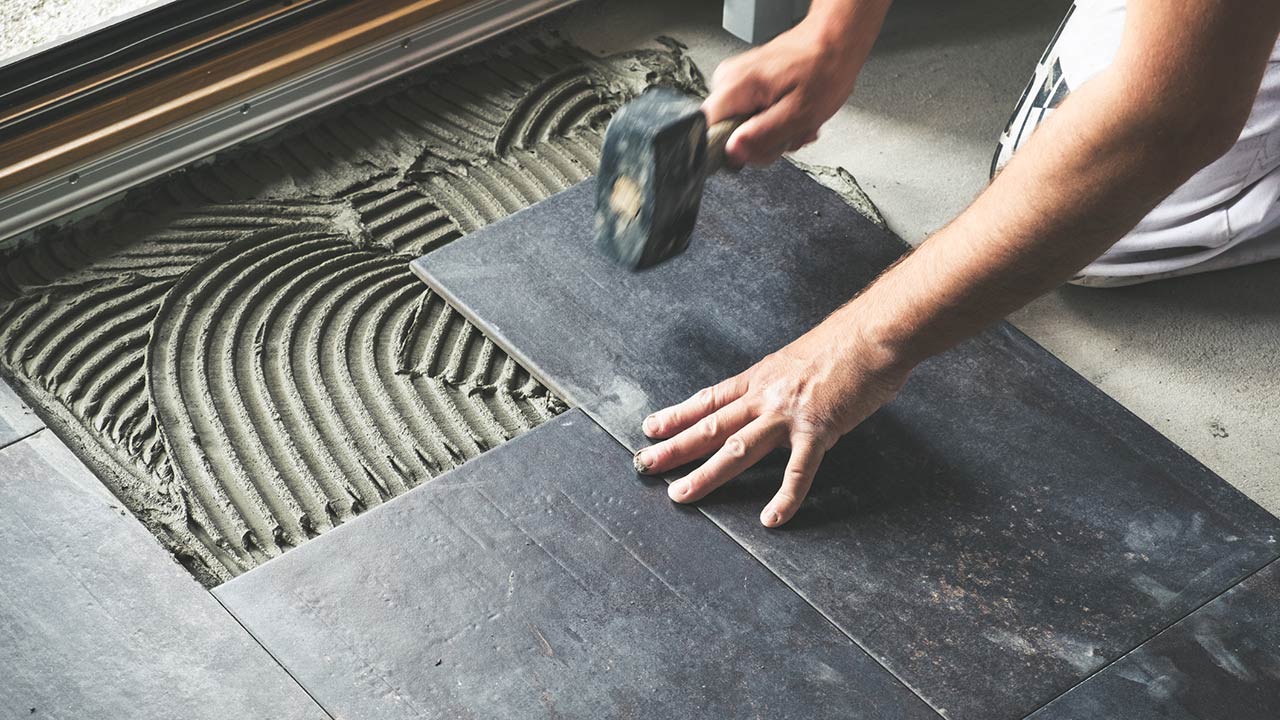 Photo of a worker carefully placing ceramic floor tiles on adhesive surface