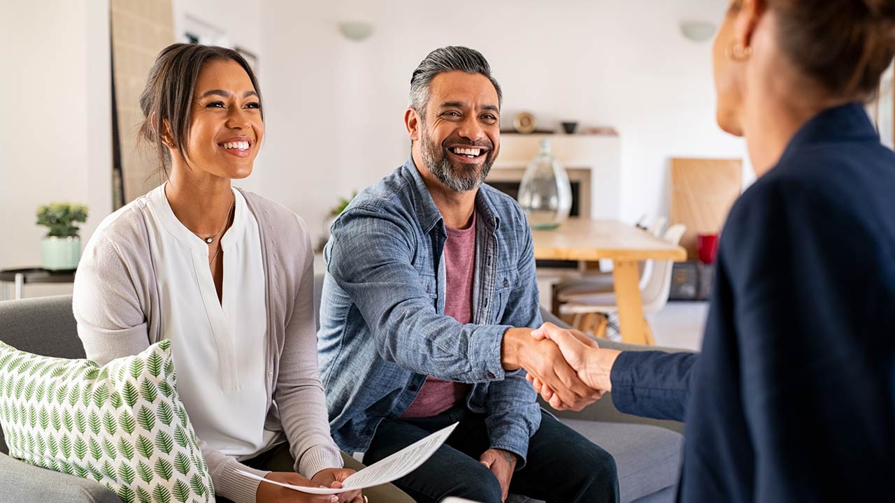 Happy smiling couple greeting broker with handshake at home