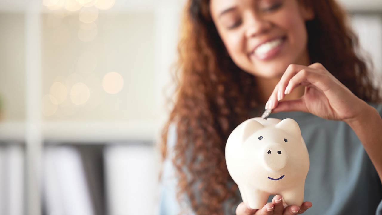 happy young mixed race woman holding a piggybank and depositing a coin as savings