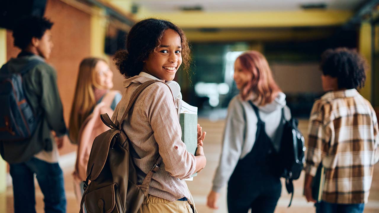 Happy African American high school student walking through hallway with her friends and looking at camera