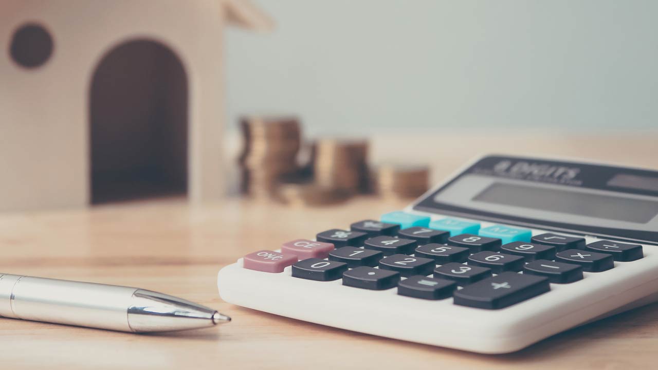 Calculator with wooden house and coins stack and pen on wood table