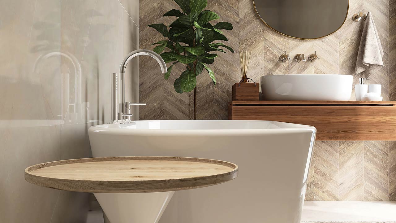 Round wooden side table, bathtub, fiddle leaf fig tree in luxury design bathroom in sunlight on beige brown tile wall
