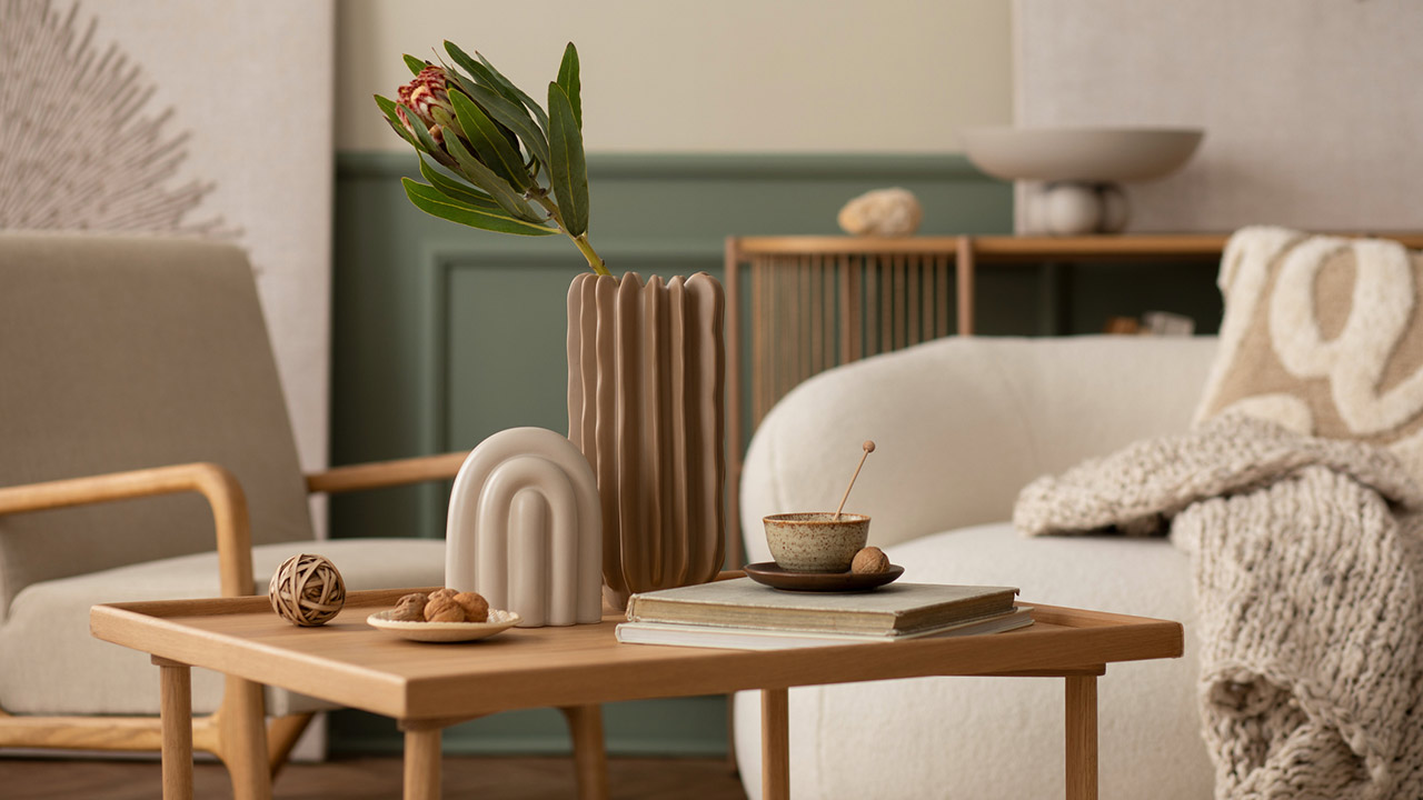 living room with boucle sofa, wooden coffee table, books, stylish sculpture, vase with leaves and personal accessories