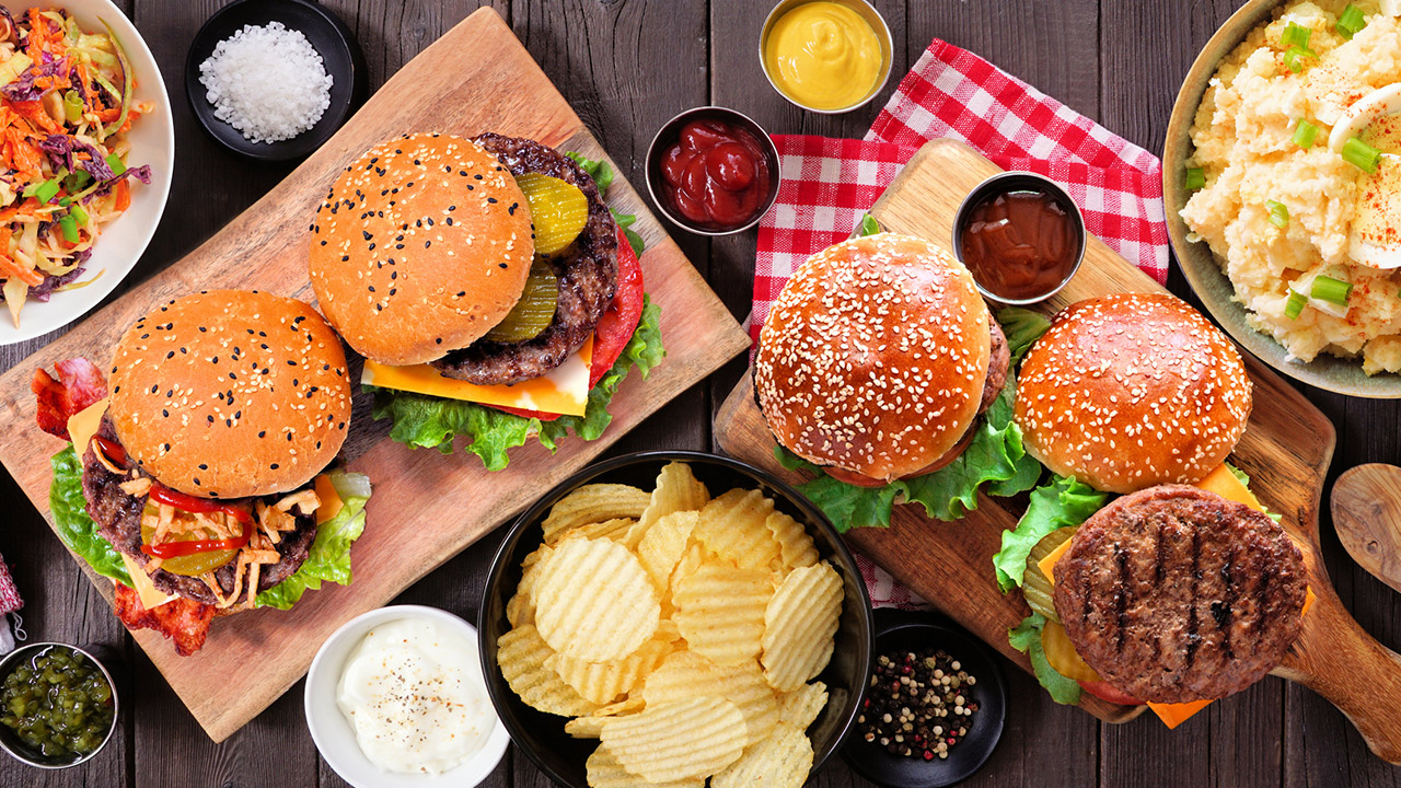 BBQ table scene with hamburgers, classic salads and snacks over dark wood stock photo