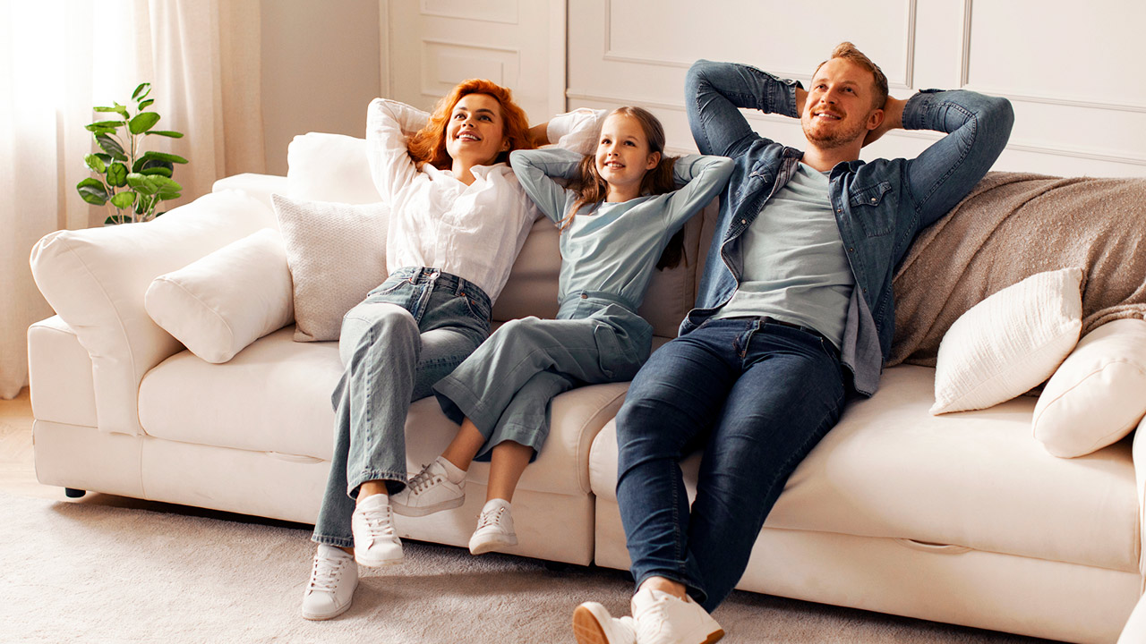 Cheerful family with child girl enjoying quality time at home in their living room, sitting on comfortable sofa, smiling and looking relaxed stock photo